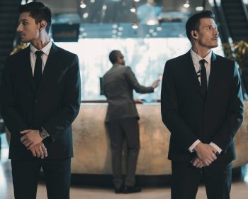 Two,Bodyguards,Waiting,For,Businessman,Standing,At,Reception,Counter